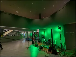 Leicht futuristisch anmutende Halle der Kulturjugendherberge München mit Blick auf eine in grünes Licht getauchte Bühne mit Instrumenten und PA