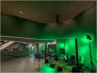 Leicht futuristisch anmutende Halle der Kulturjugendherberge München mit Blick auf eine in grünes Licht getauchte Bühne mit Instrumenten und PA